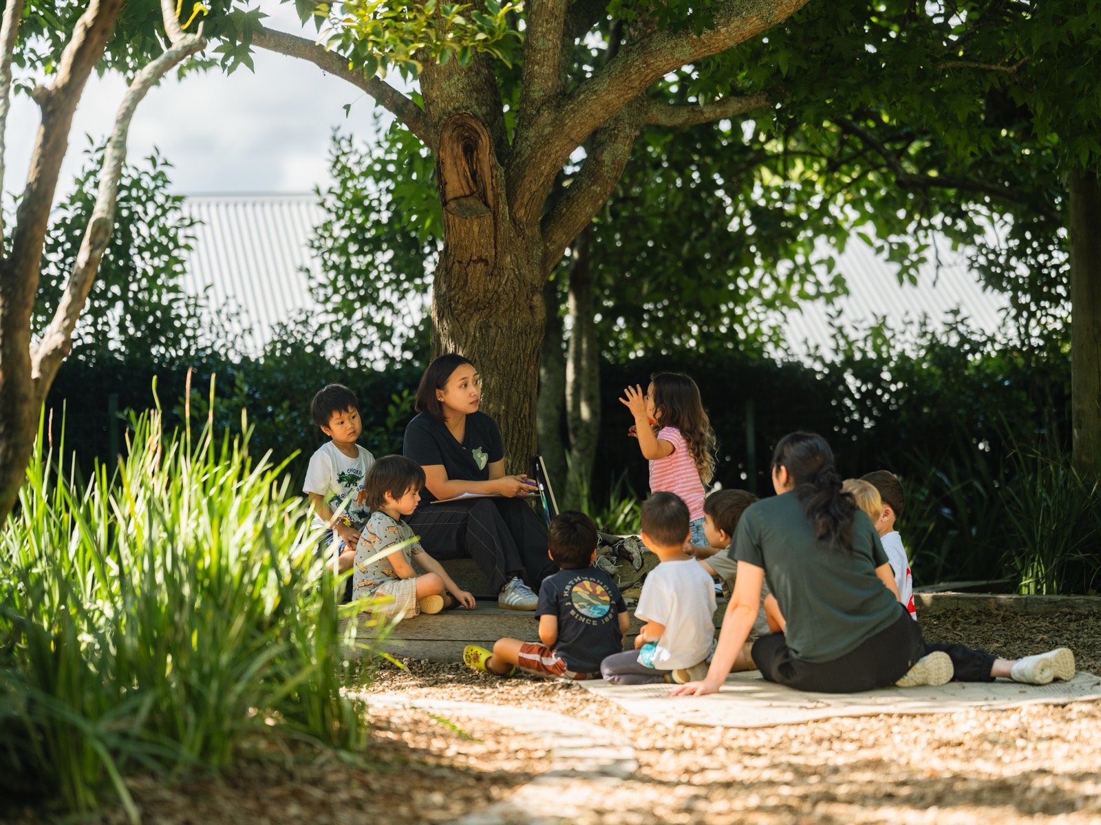 A teacher with a group of children gathered under a tree at a Bear Park centre
